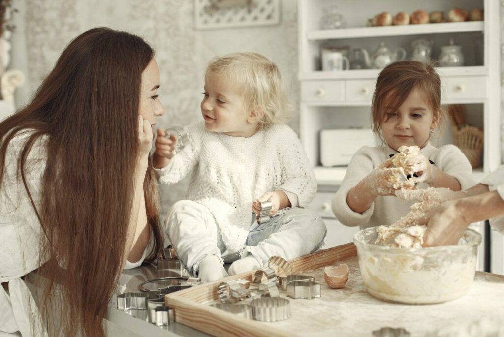 Maman cuisinant avec ses deux enfants dans une cuisine lumineuse, éducation alimentaire en famille