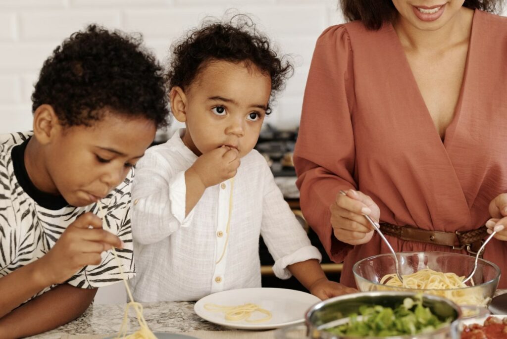 Enfants mangeant des spaghettis en famille dans une cuisine lumineuse