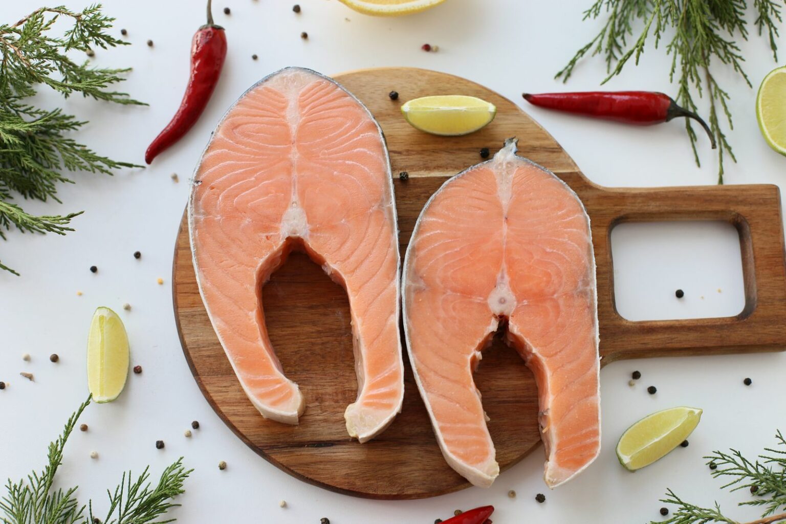 Deux pavés de saumon crus sur une planche avec citron, aneth et poivre
